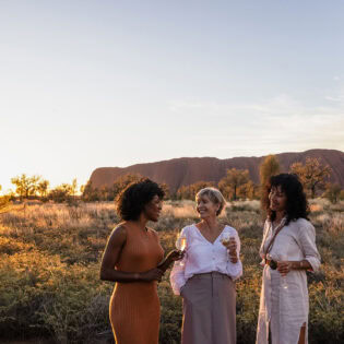 three women drinking champagne in front of uluru