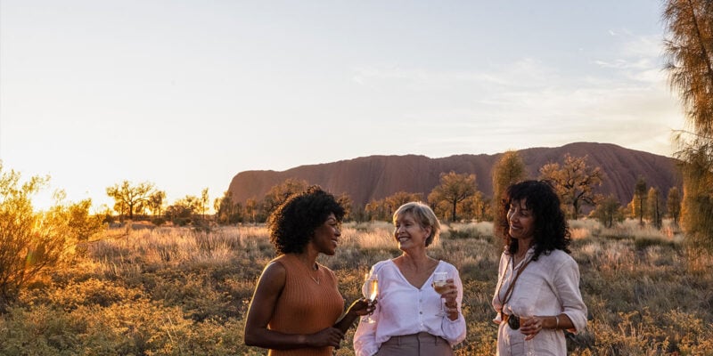 three women drinking champagne in front of uluru