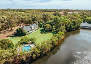 A photo of a white building and a swimming pool surrounded by trees and a river viewed from above.