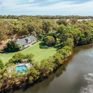 A photo of a white building and a swimming pool surrounded by trees and a river viewed from above.