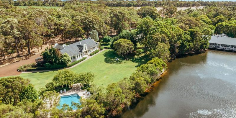 A photo of a white building and a swimming pool surrounded by trees and a river viewed from above.