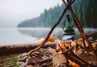 Campfire with a vintage kettle next to the beautiful lake.