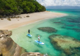 an aerial shot of two people stand-up paddling on the clear turquoise waters of Nudey Beach, Fitzroy Island