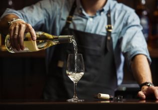 a bartender pouring white wine into a long-stemmed glass