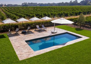 an outdoor pool with umbrellas and sun loungers surrounded by an expansive vineyard in Le Mas, Barossa Valley